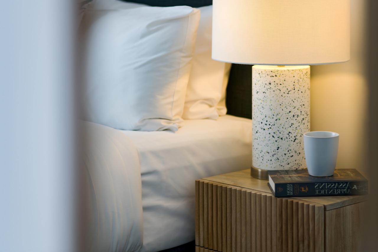 Bedside table with terrazzo lamp, book and coffee against crisp white linen