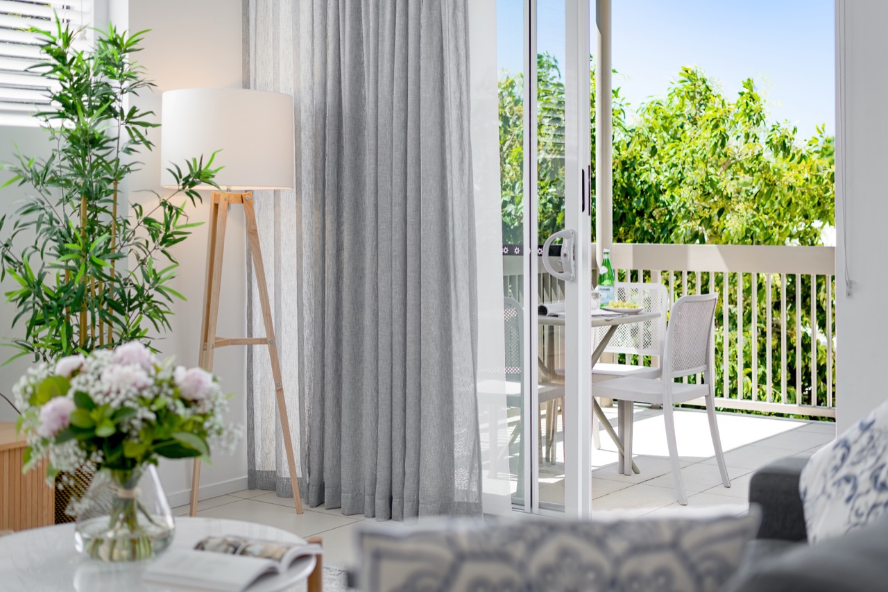 Living area with a floor lamp and fresh flowers opening through sliding doors to a leafy balcony